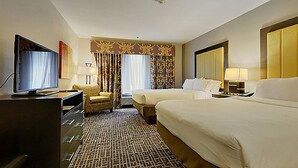 A hotel room with two beds, a television, a desk with a chair, and a patterned carpet.
