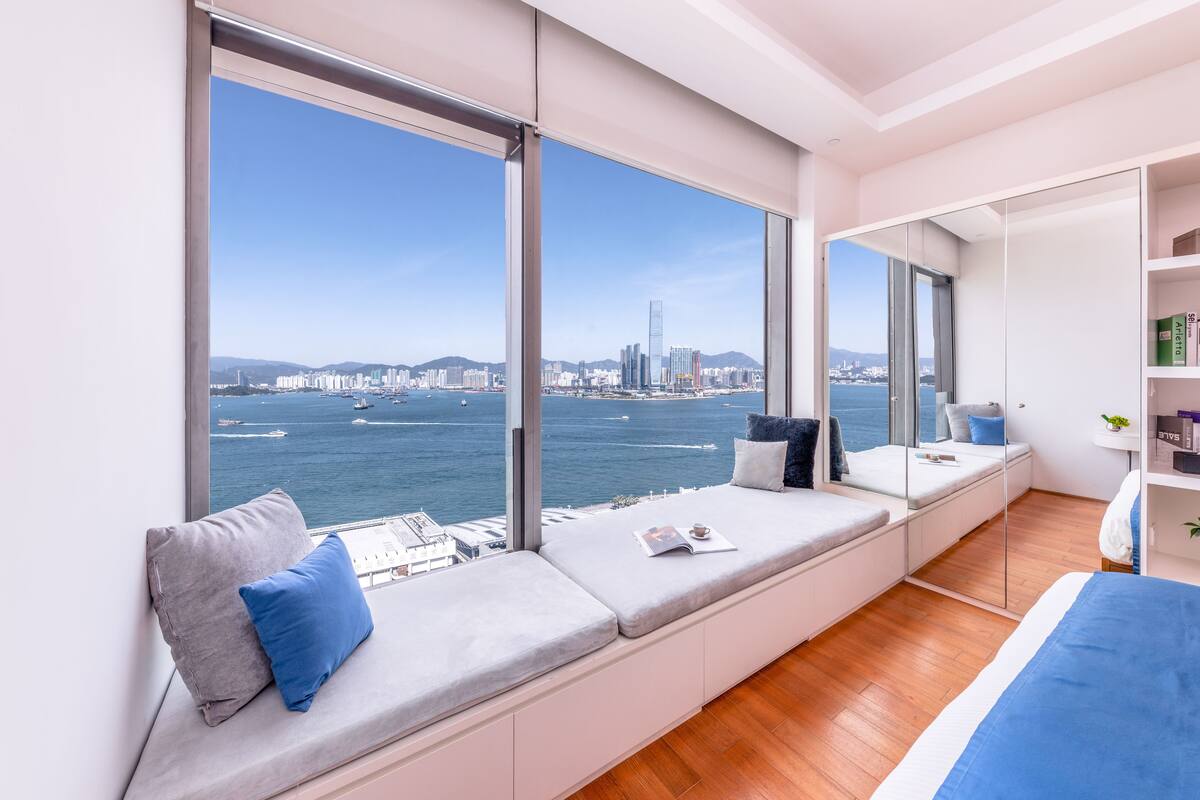 A modern room with large windows offering a city view, a built-in bench with cushions, and a wooden floor.