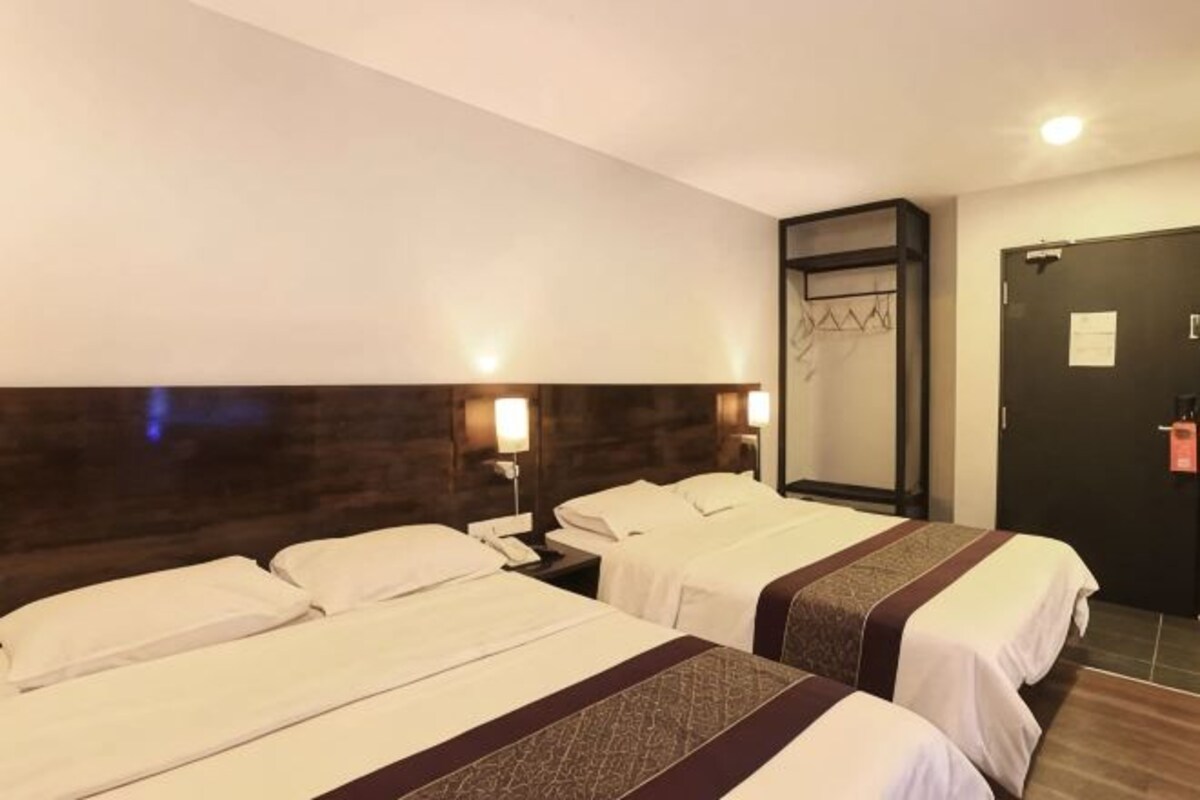 Habitación de hotel con dos camas, cabecera oscura, lámparas de noche, una puerta con un cartel y suelo de madera.