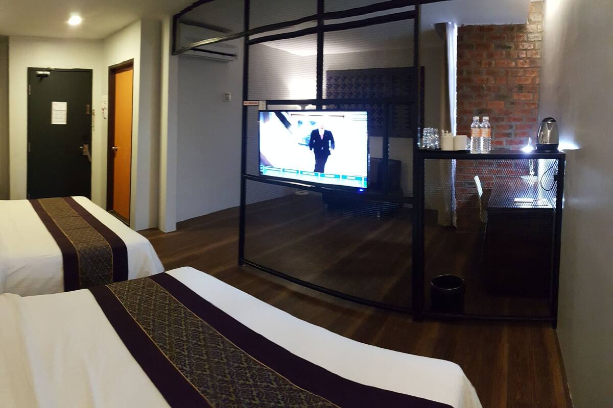 A hotel room with two beds, a TV, a small table with a kettle, and a glass of water.