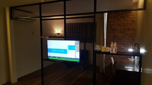 A room with a TV displaying stock market data, a brick wall, and a table with bottles and glasses.