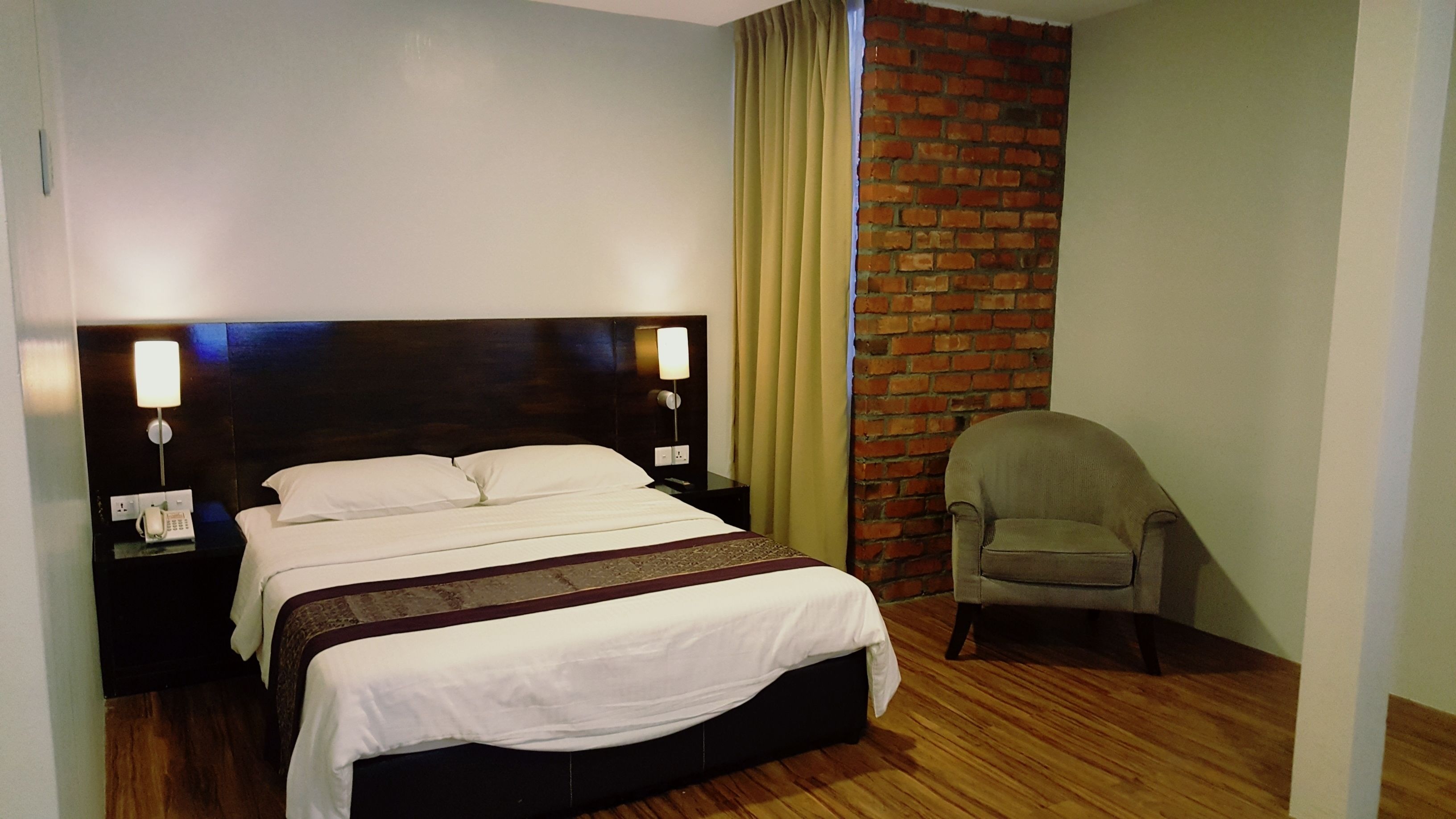 A hotel room with a bed, a chair, a brick wall, and a curtain.
