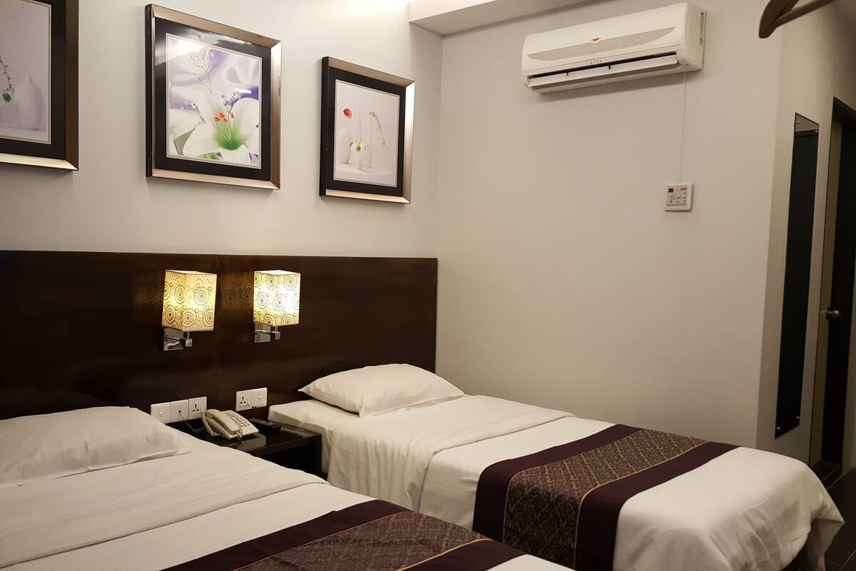 A hotel room with two beds, a headboard, wall-mounted lamps, framed artwork, an air conditioning unit, and a telephone.