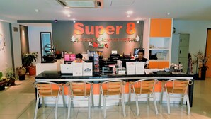 A hotel reception desk with a large sign reading "Super 8" and "Merry Christmas." There are several chairs in front of the desk, a computer, and a suggestion box.