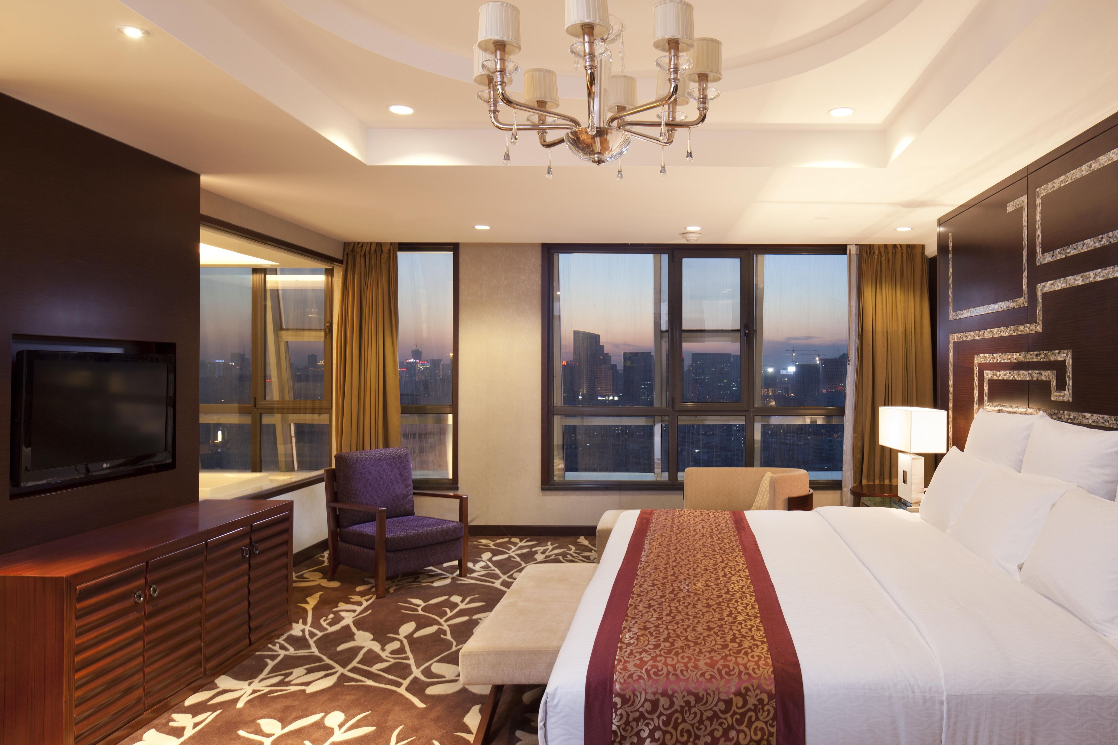 Habitación de hotel con una cama grande, televisión, zona de estar y vistas a la ciudad.