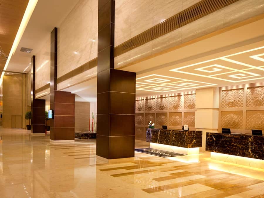 Un vestíbulo de hotel con una recepción, una columna grande y un muro con diseño.