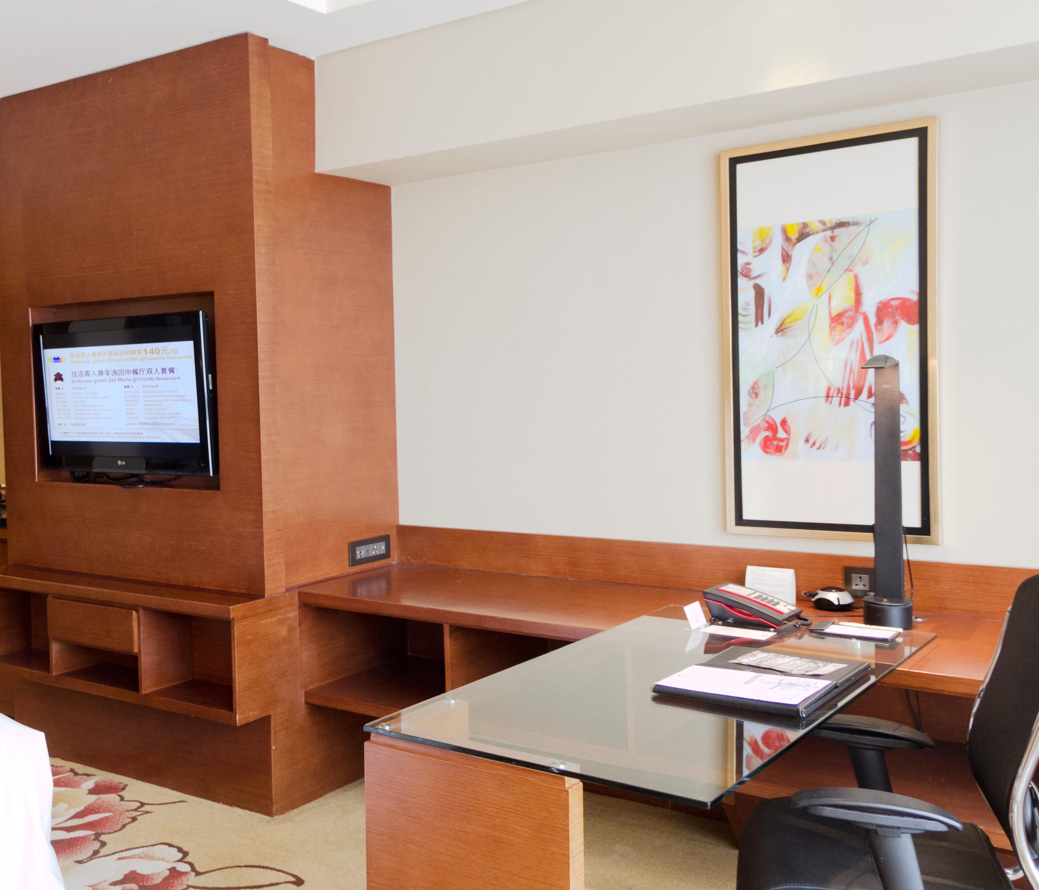 Eine Hotelhalle mit einer Rezeption, einem Flachbildfernseher, einem gerahmten abstrakten Gemälde und einem Teppich mit einem floralen Muster.
