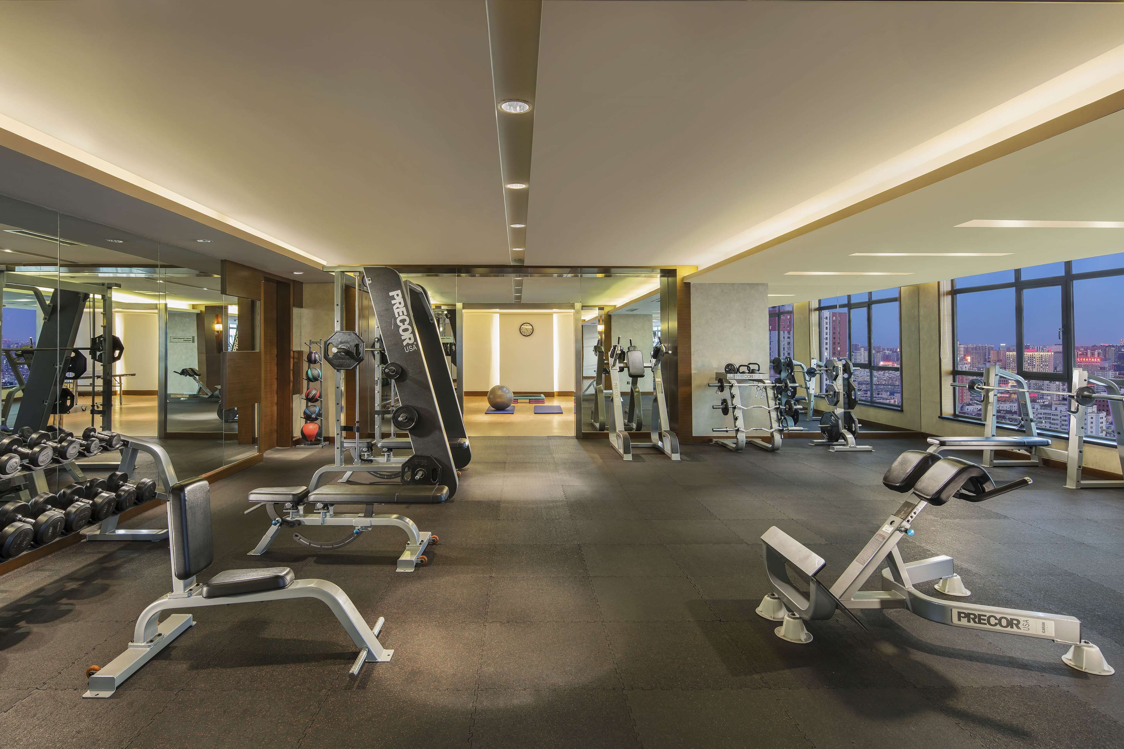 A modern gym with various exercise equipment, large windows offering city views, and a spacious layout.