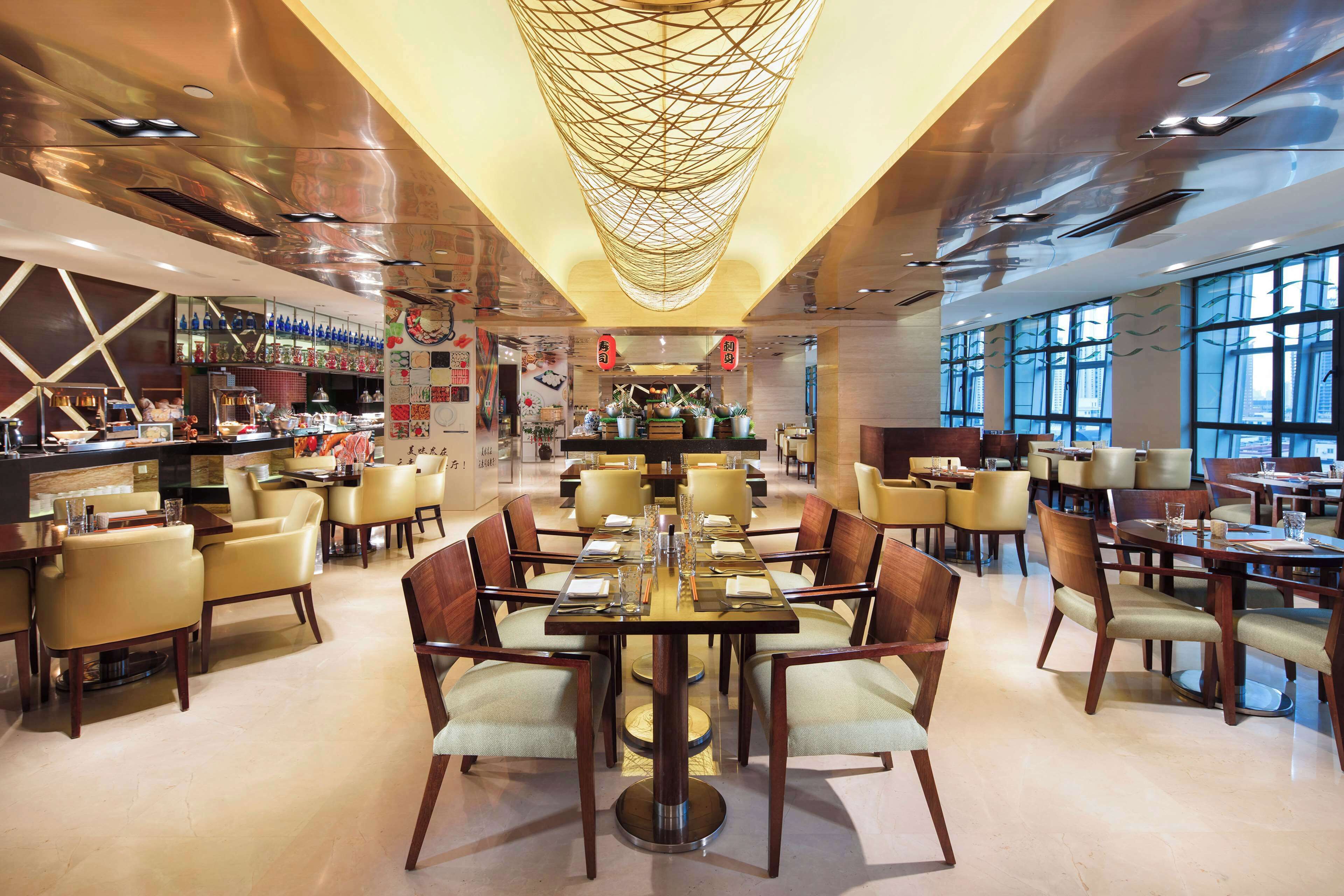 Un restaurante espacioso con numerosas mesas y sillas, una zona de bar y grandes ventanales que dejan entrar luz natural.