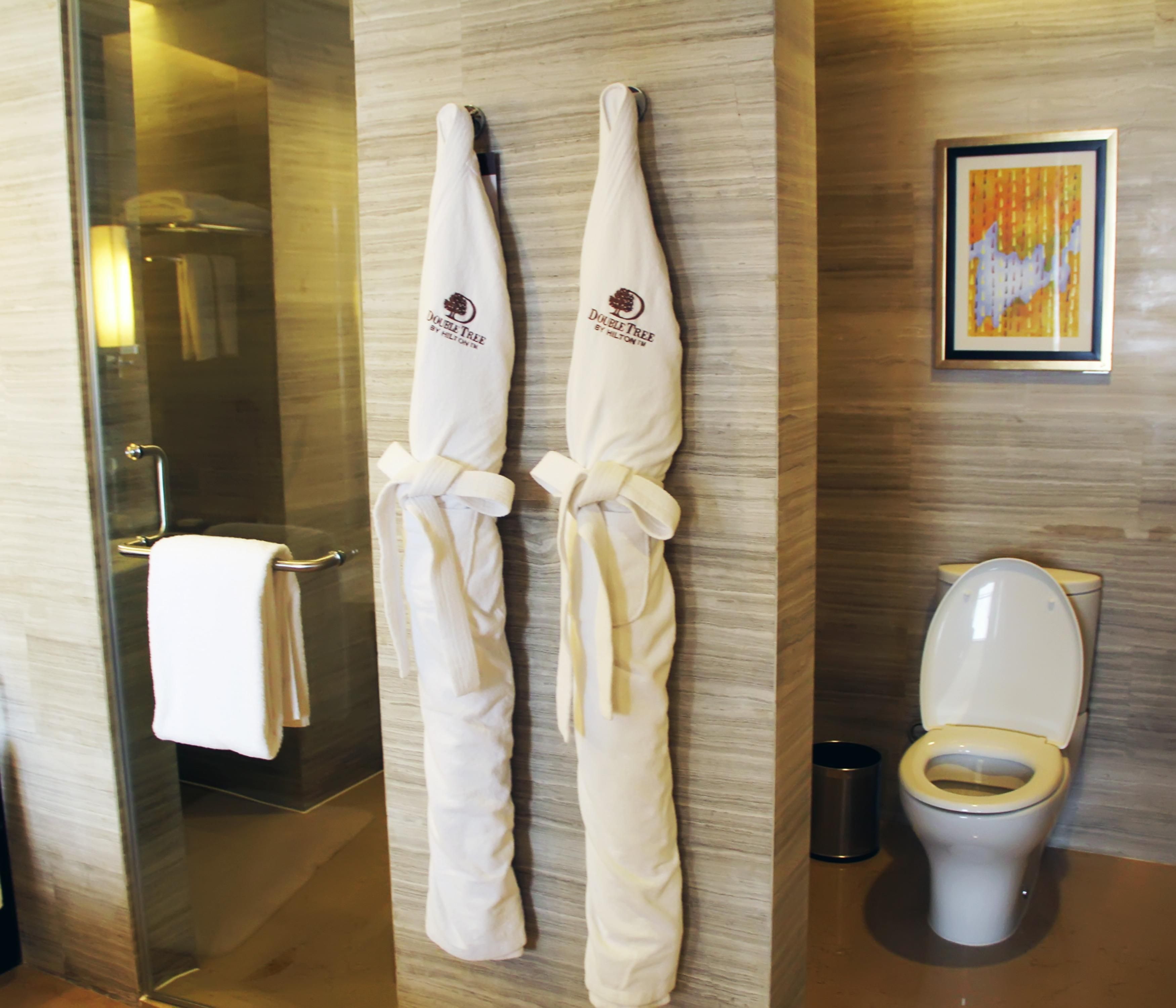 A bathroom with a glass shower enclosure, a toilet, and two towels hanging on the wall.