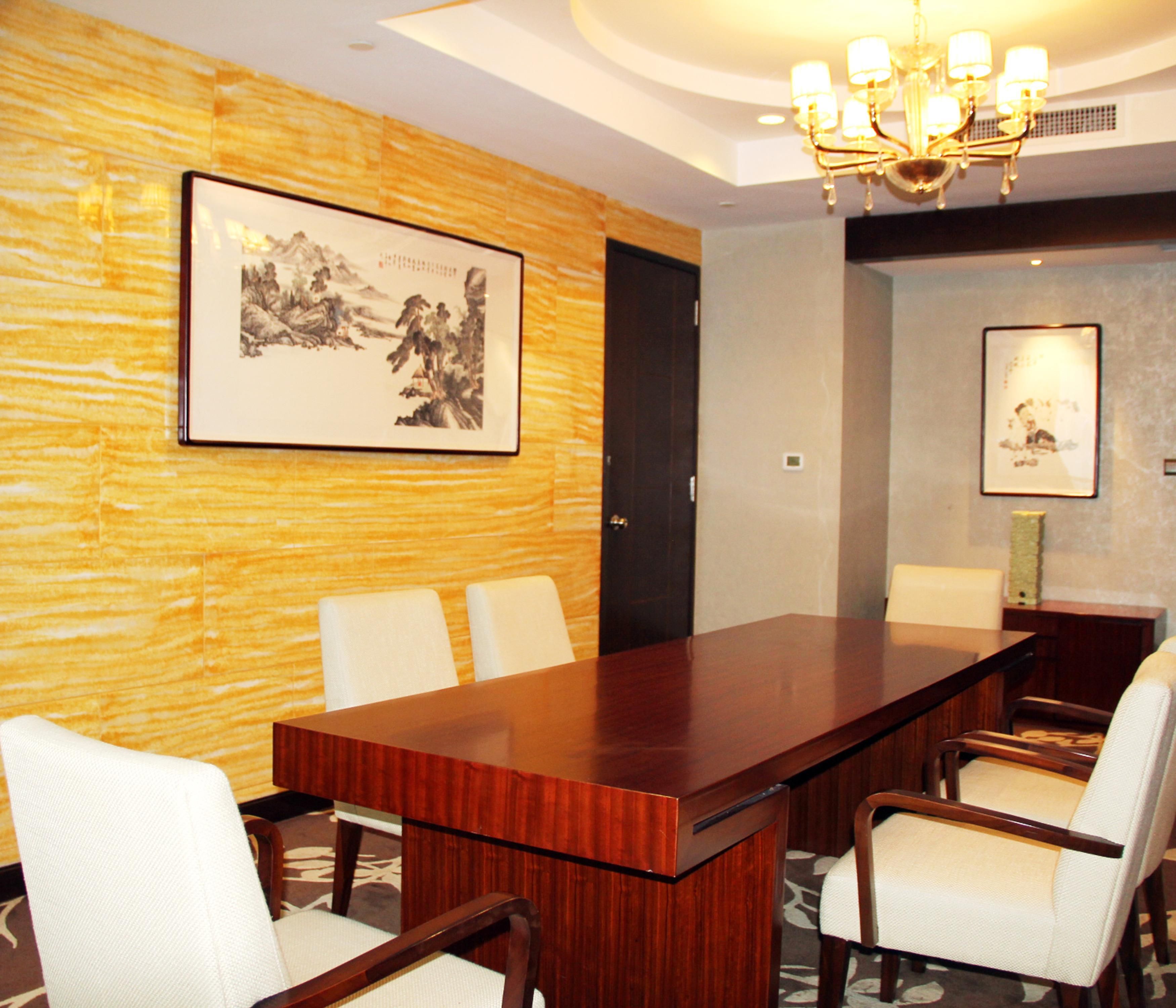 A conference room with a long wooden table, white chairs, a chandelier, and framed artwork on the walls.