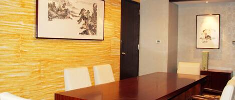 A conference room with a long wooden table, white chairs, a chandelier, and framed artwork on the walls.