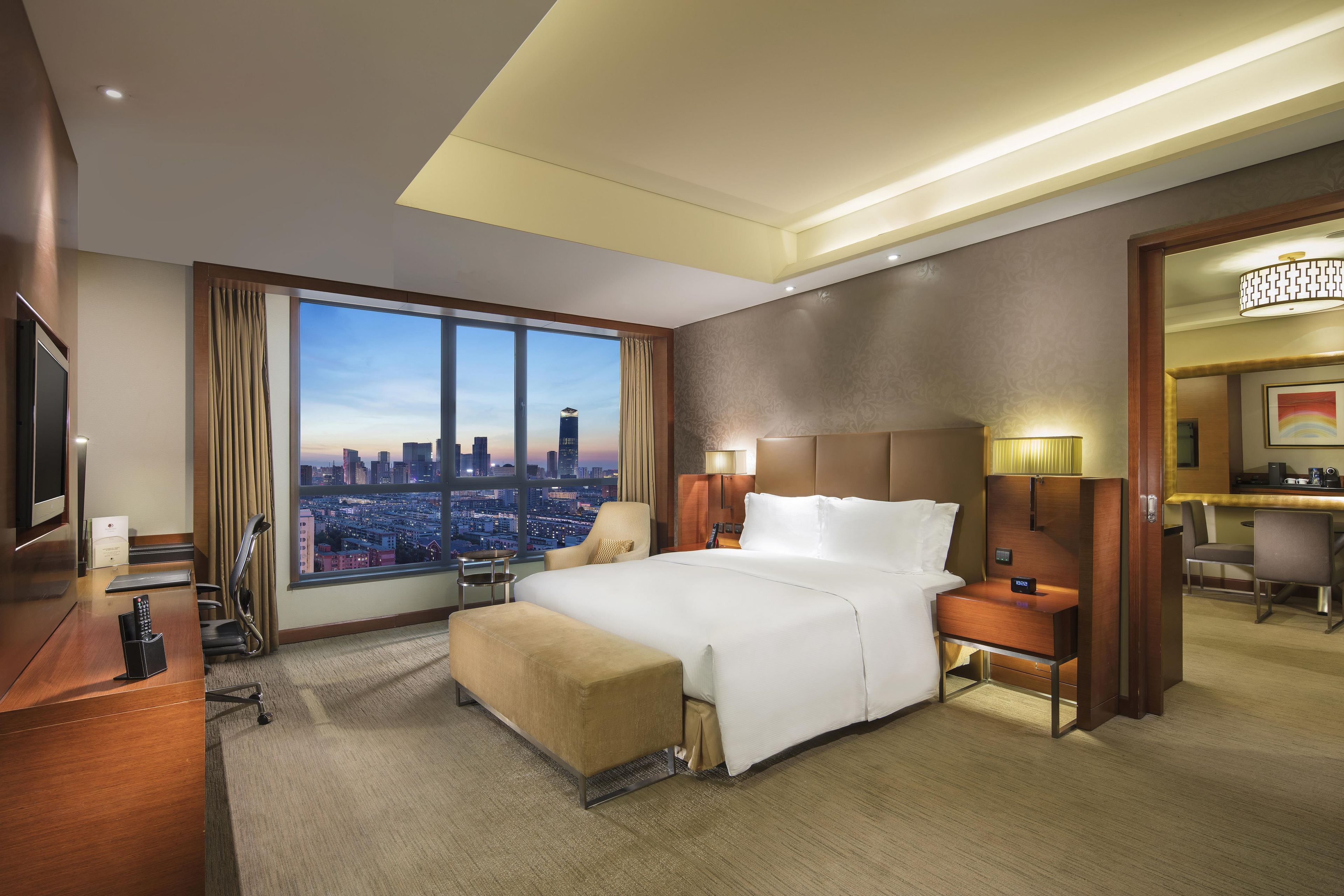 Een hotelkamer met een groot raam, een bed, een bureau en een stoel.
