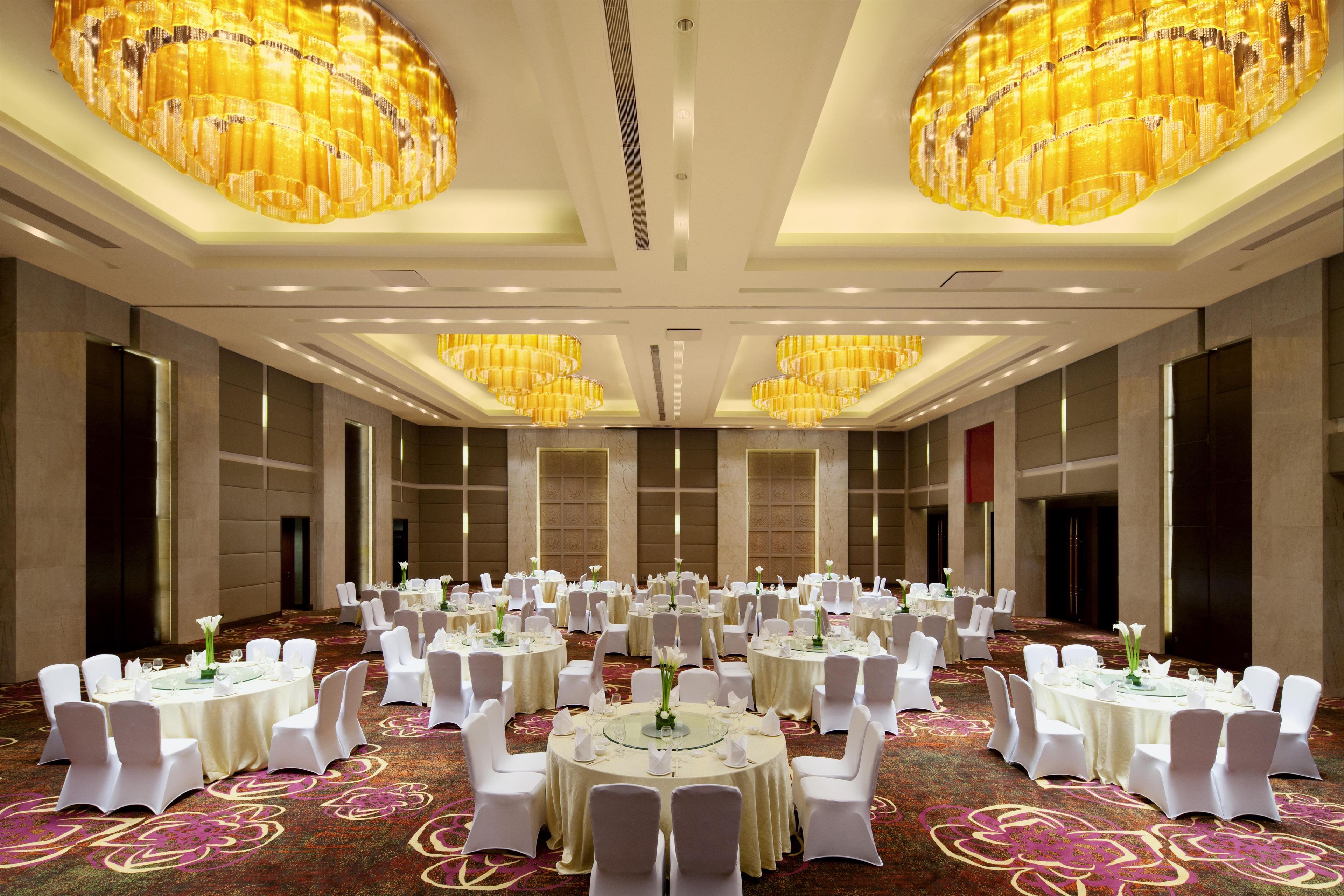 A large banquet hall with round tables, white chairs, and chandeliers.
