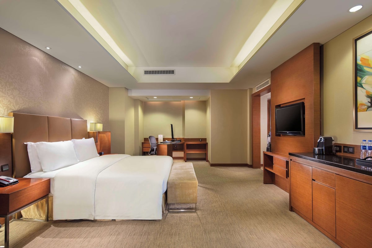 A hotel room with a large bed, a desk, a TV, and a minibar.