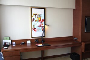 Un mostrador de hotel con una computadora portátil, un teléfono, un ratón, una lámpara y un cuadro abstracto enmarcado en la pared.