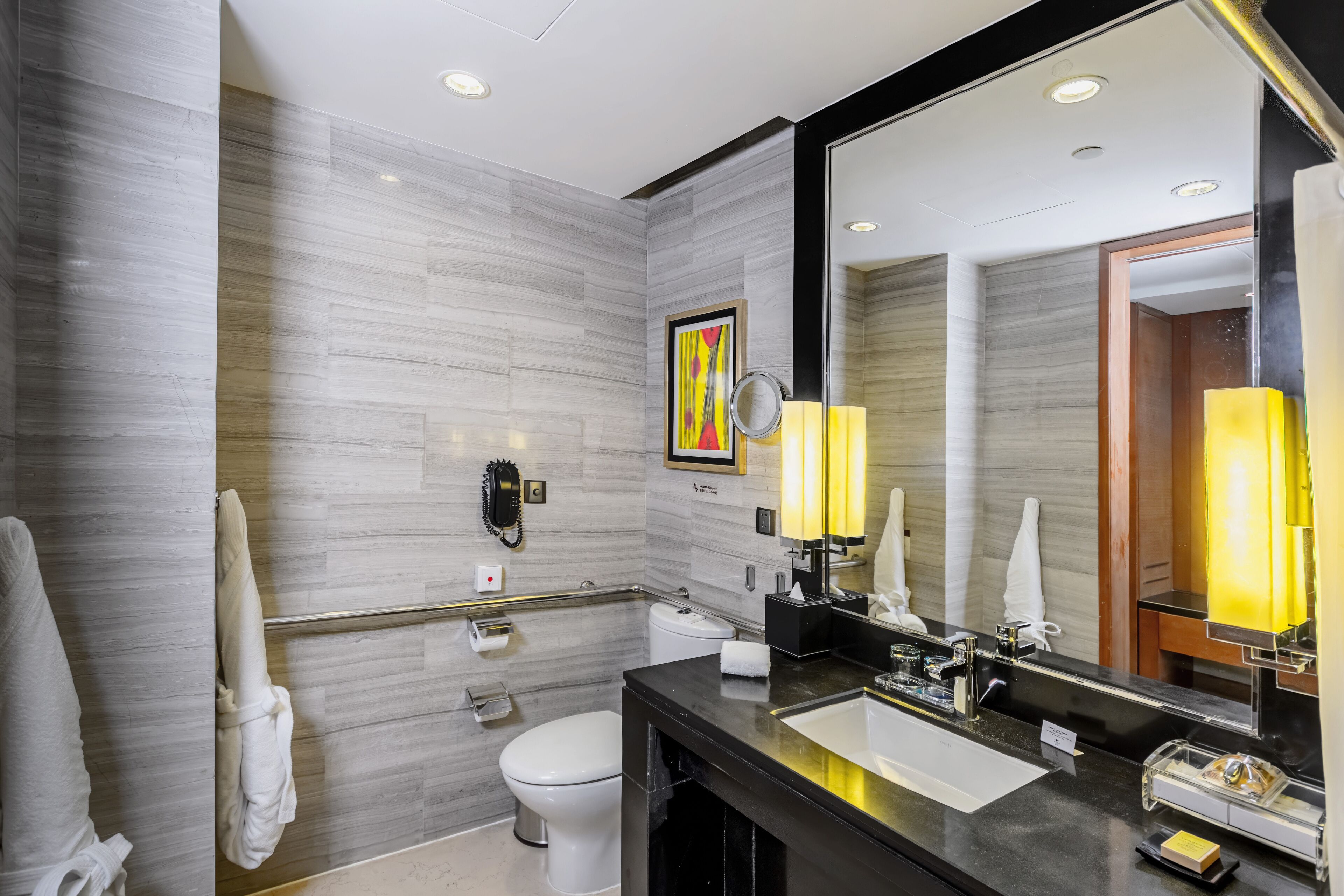 Un bagno moderno con una parete in marmo, un lavandino nero, uno specchio e un water.