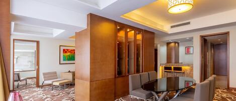 A modern hotel lobby with a glass table, cushioned chairs, a patterned carpet, and a large wooden partition.
