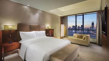 A hotel room with a large bed, a sofa, a city view, and a TV.