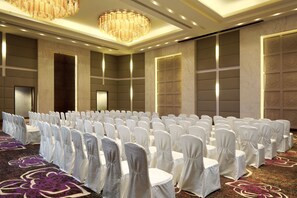 Un salón de conferencias con filas de sillas blancas, suelo alfombrado y una araña de cristal.