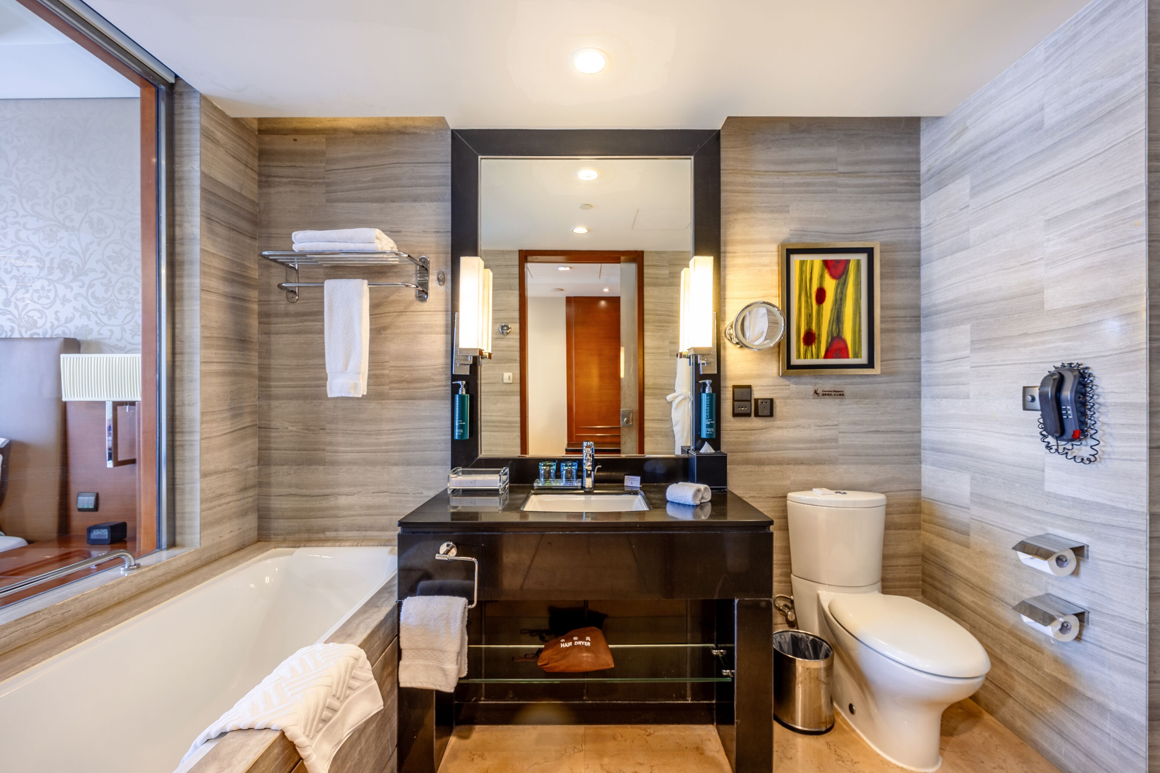Un baño moderno con bañera, lavamanos e inodoro. Hay un espejo sobre el lavamanos y un perchero en la pared.