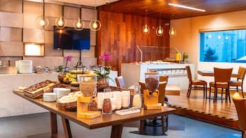 A modern hotel breakfast area with a buffet table, seating, and a view of the city.