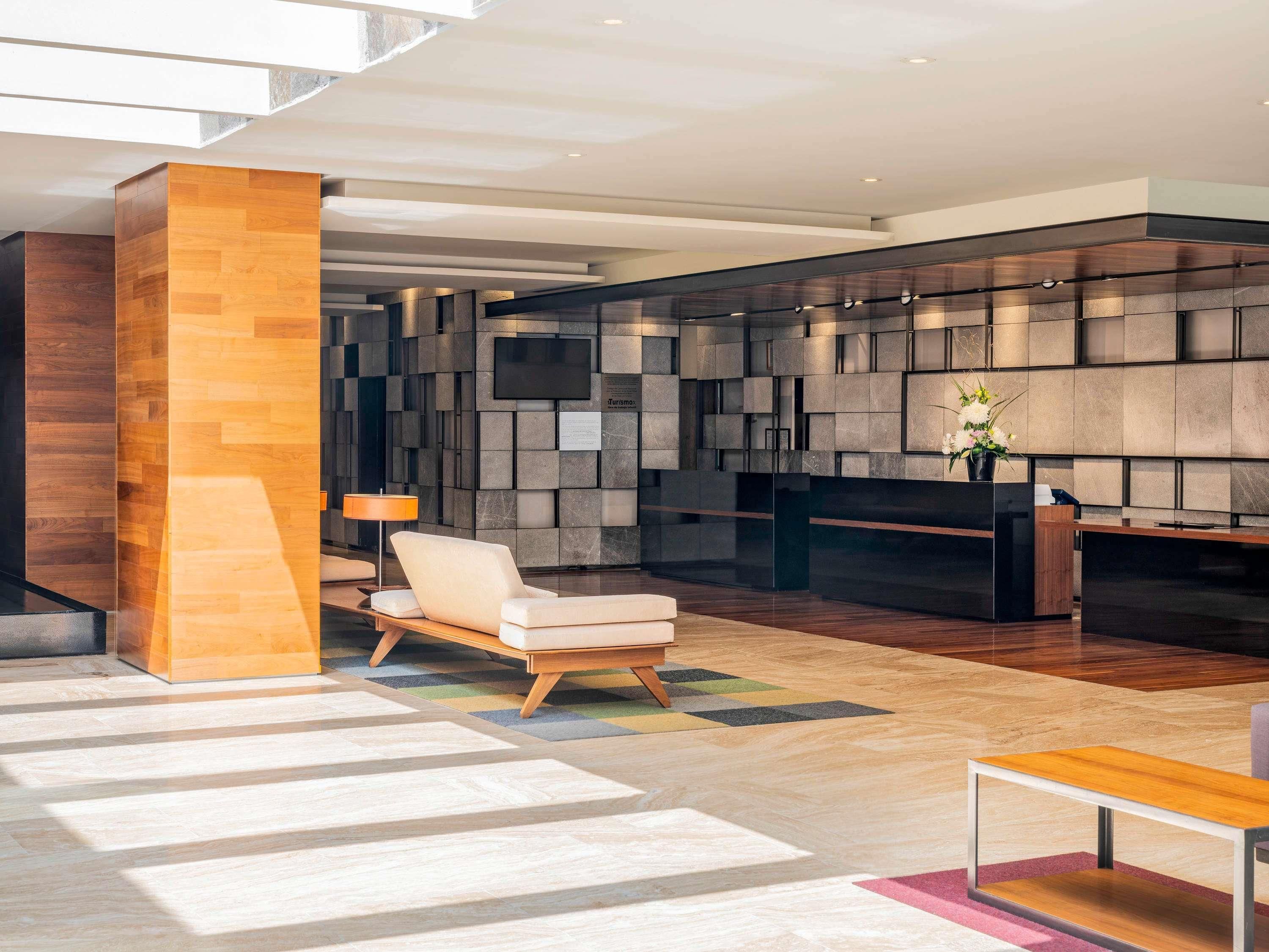 Un lobby moderno con mostrador de recepción, área de estar y una pared grande con diseño geométrico.