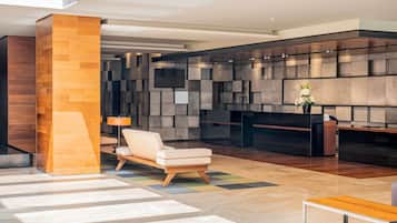 Un lobby moderno con mostrador de recepción, área de estar y una pared grande con diseño geométrico.
