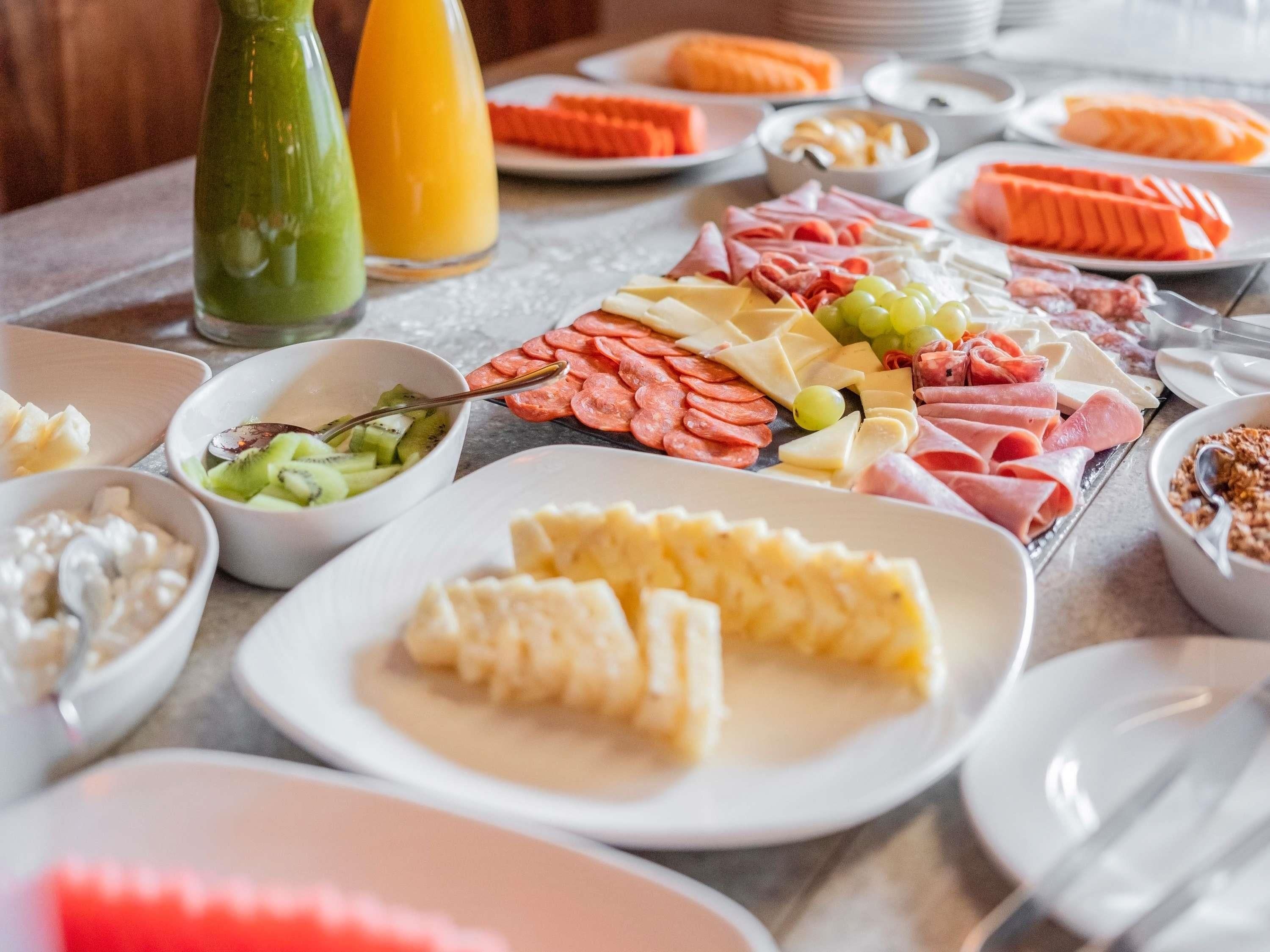 A breakfast buffet with various cheeses, meats, fruits, and a green smoothie.