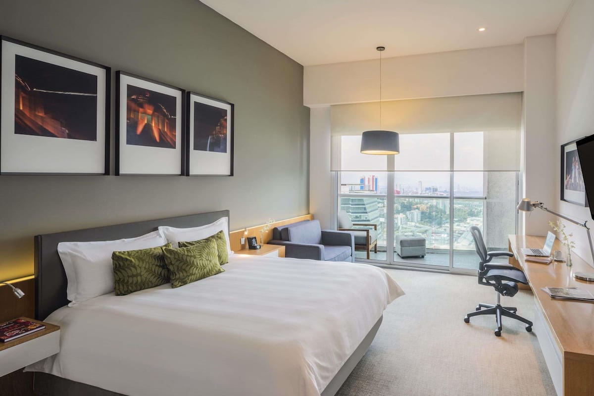A hotel room with a large bed, a desk, a chair, a sofa, and a view of the city.