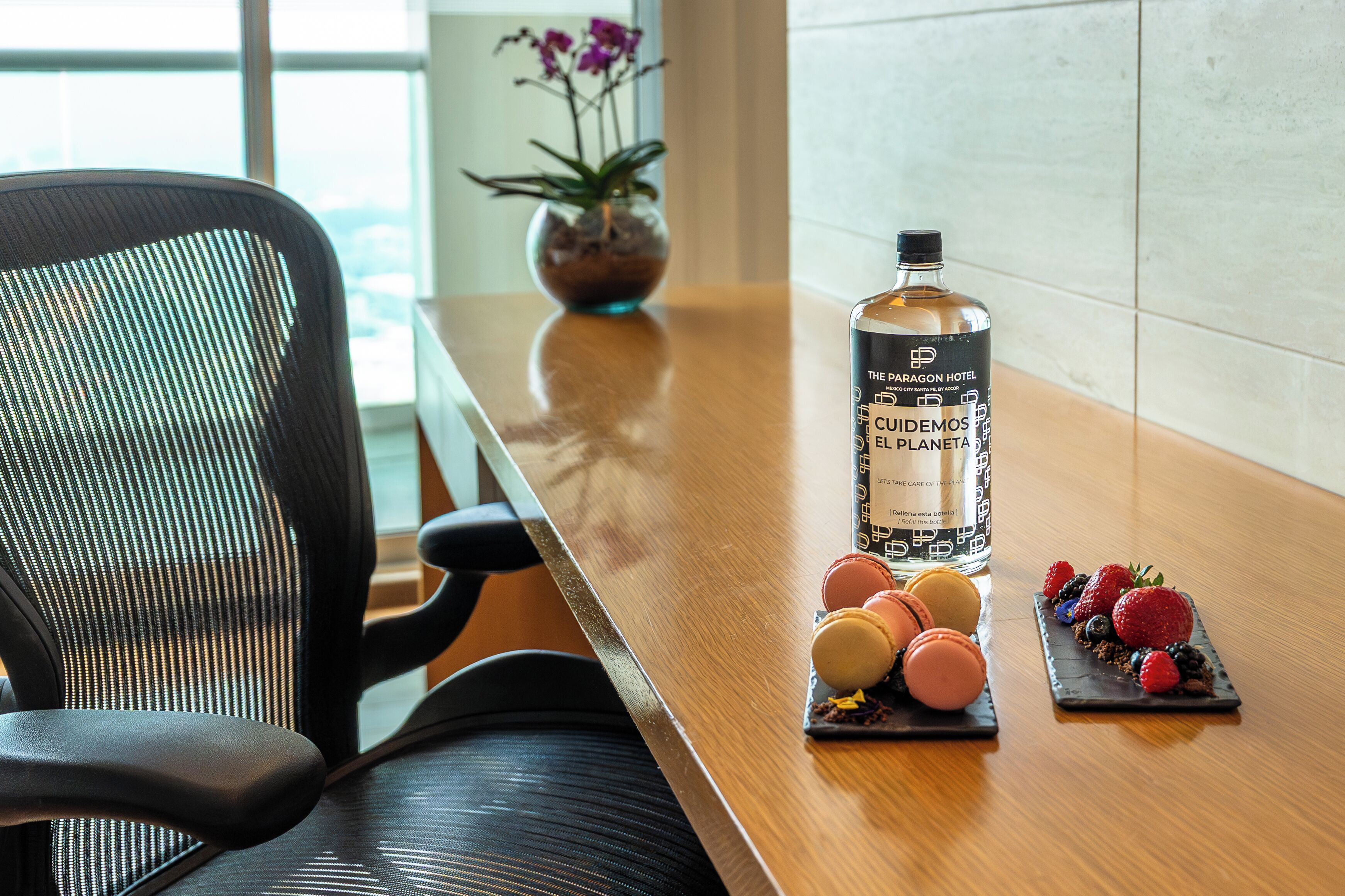 A wooden table with a bottle of El Planeta rum, macarons, and a small potted plant.
