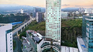 A high-rise building with a modern glass facade, surrounded by other buildings and a highway. - The Paragon Hotel Mexico City Santa Fe By Accor (Mexico City)