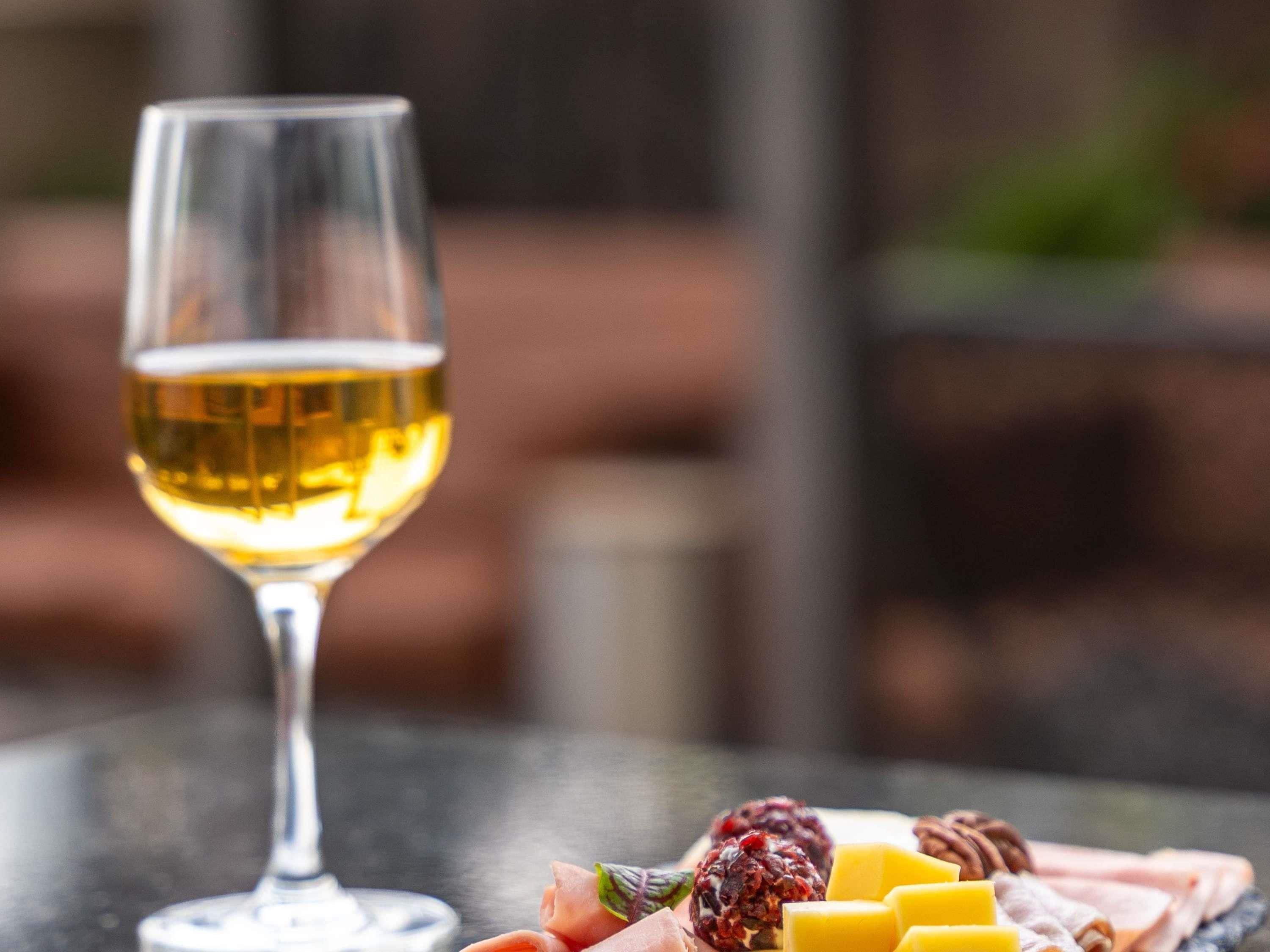 Ein Glas Weißwein und eine Wurstplatte mit verschiedenen Käsesorten, Früchten und Fleisch.