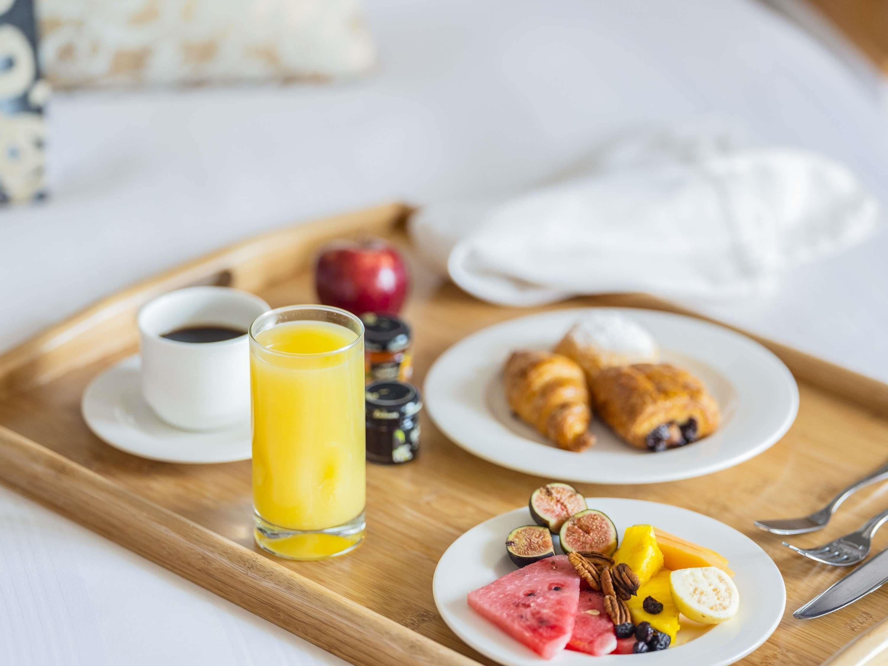 Un vassoio per la colazione con croissant, fichi, anguria, noci pecan e un bicchiere di succo d'arancia.