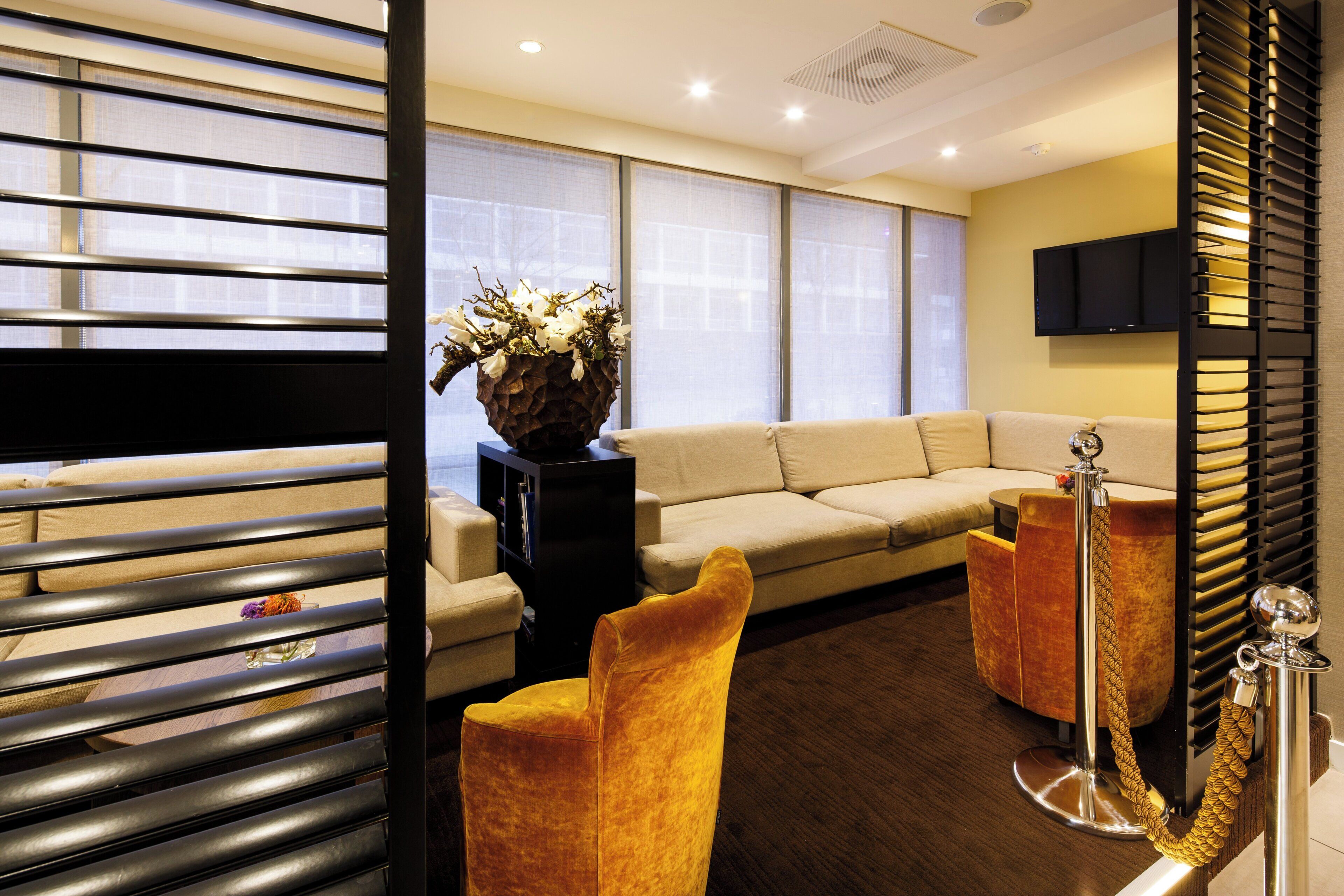 A modern hotel room with a sofa, a small table, a decorative vase, and a television mounted on the wall.