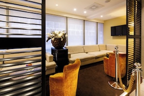 Una habitación de hotel moderna con sofá, una mesita, un florero decorativo y un televisor montado en la pared.