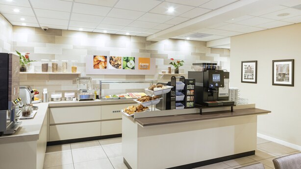 A modern hotel reception area with a self-service breakfast bar, coffee machines, and a clean, tiled floor. - Holiday Inn Express Amsterdam - South by IHG (Amsterdam)