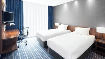A hotel room with two beds, a desk with a TV, a chair, and a patterned carpet.