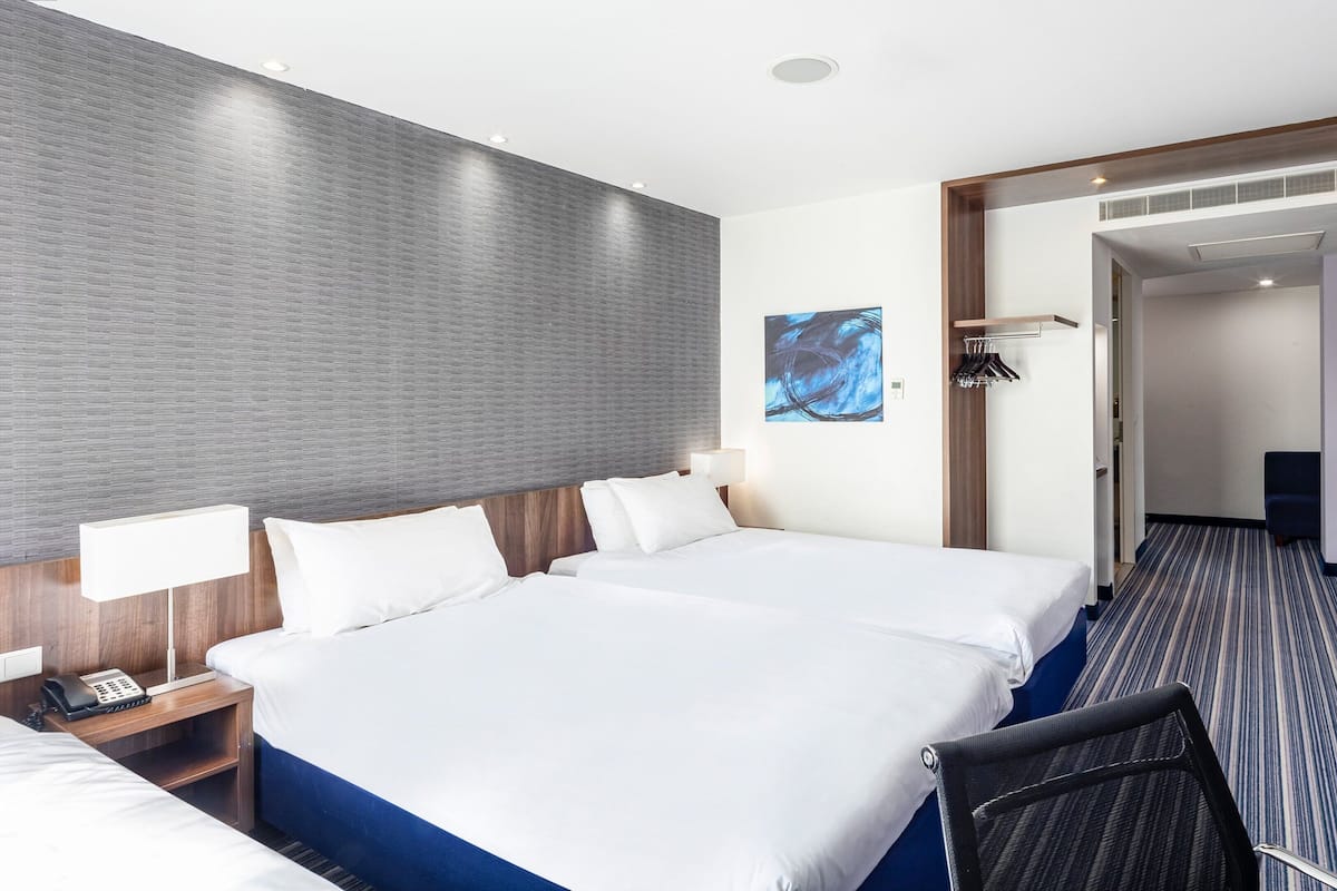 Une chambre d’hôtel avec un grand lit, des tables de chevet, un bureau, une chaise, une armoire et une salle de bain visible à travers une porte ouverte.