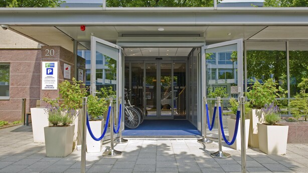 A hotel entrance with a blue carpet, glass doors, and a number 20 sign. - Holiday Inn Express Amsterdam - South by IHG (Amsterdam)
