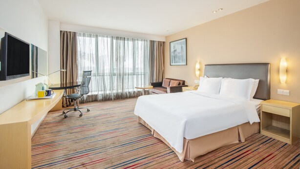 Una habitación de hotel con una cama grande, un escritorio con una silla, un televisor y una ventana con cortinas.