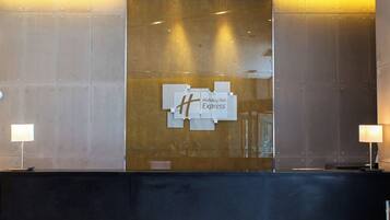A reception desk with a Holiday Inn Express sign, a glass partition, and two lamps.