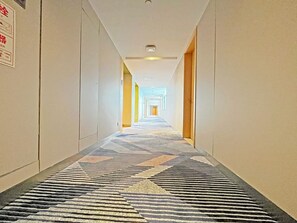 Un pasillo de hotel con alfombra estampada, puertas a ambos lados y una pared de color claro.