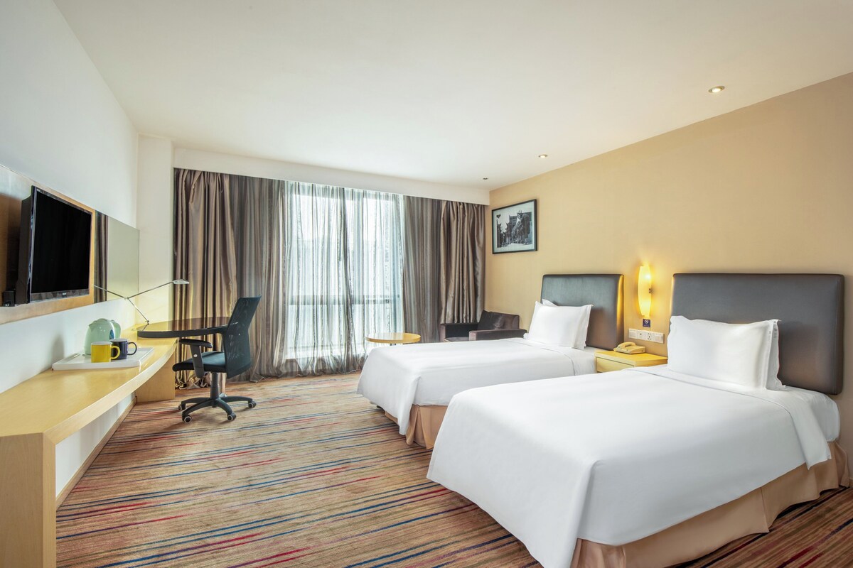A hotel room with two beds, a desk with a chair, a television, and a window with curtains.