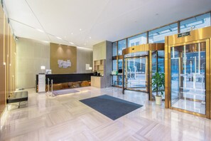 Un moderno vestíbulo de hotel con una recepción, un área de espera y una puerta giratoria que da al exterior.