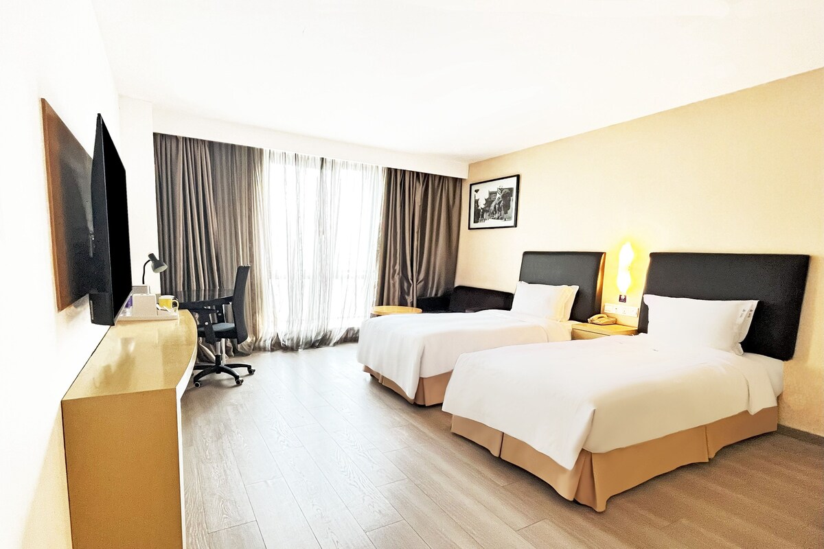 A hotel room with two beds, a desk with a chair, a TV, and a window with curtains.