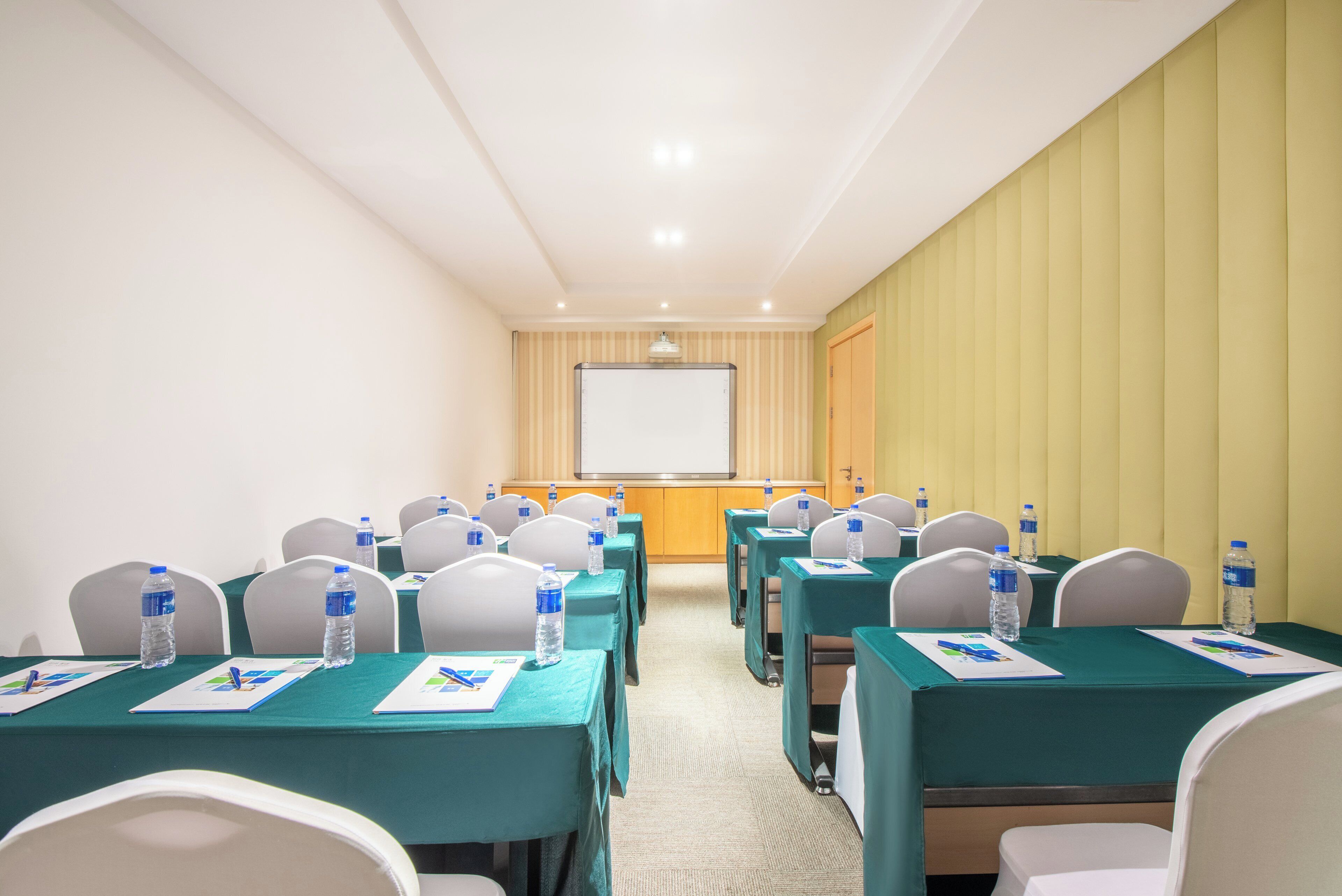 Un salón de conferencias con filas de mesas, sillas y botellas de agua.