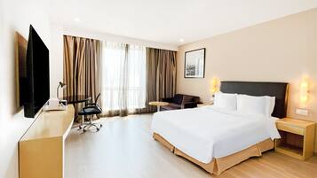 Hotellihuone, jossa on sänky, työpöytä, tuoli, televisio ja verhot.