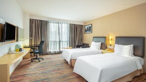 Habitación de hotel con dos camas, un escritorio con silla, televisor y ventana con cortinas.