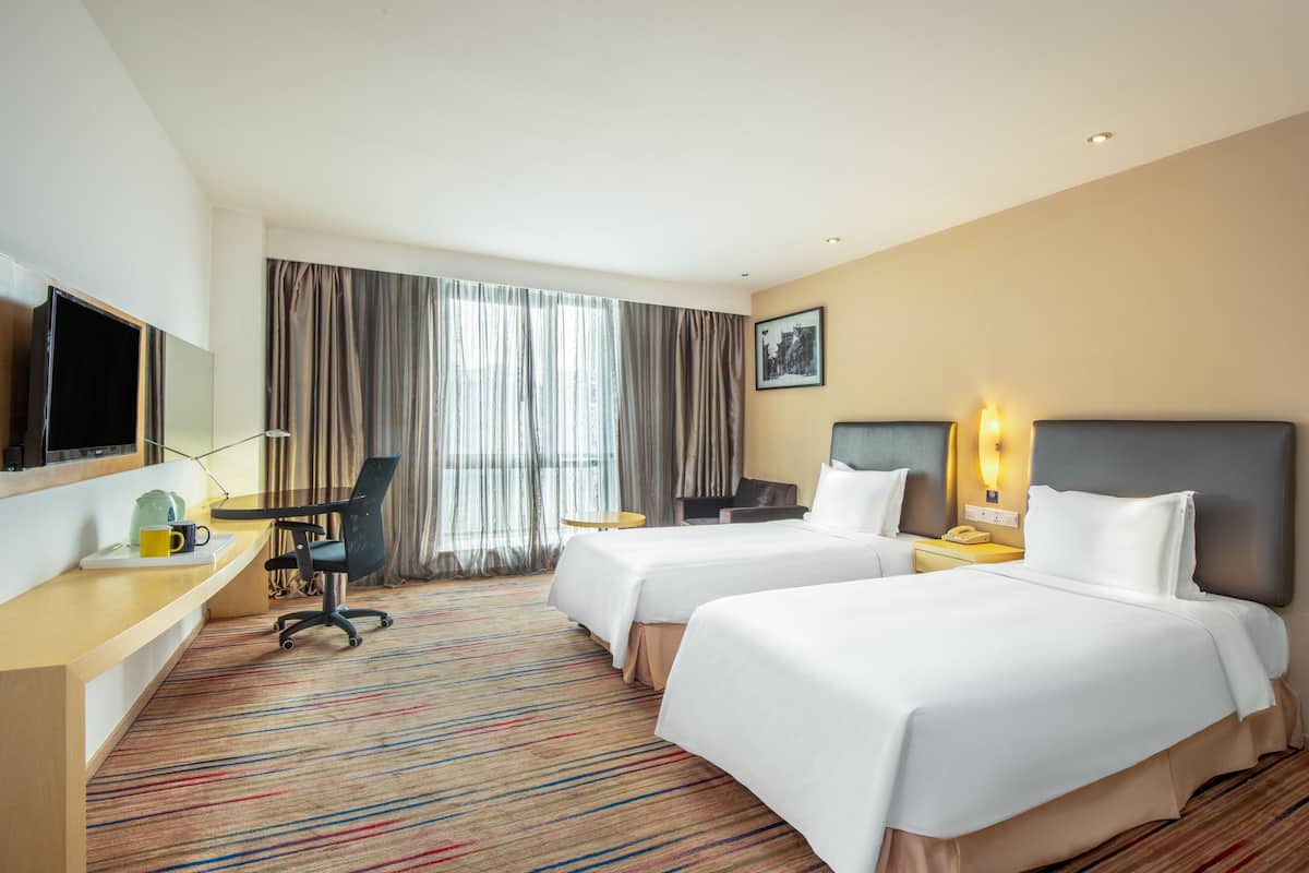 A hotel room with two beds, a desk with a chair, a television, and a window with curtains.